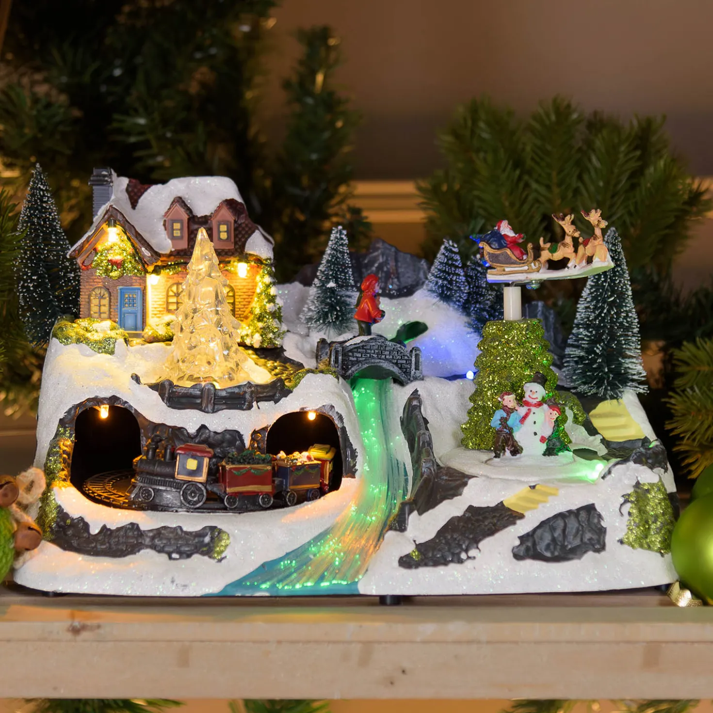Villaggio di Natale con Paesaggio Innevato, Trenino e Babbo su Slitta rotanti, Ruscello fibre ottiche, h 18 cm, musiche natalizie